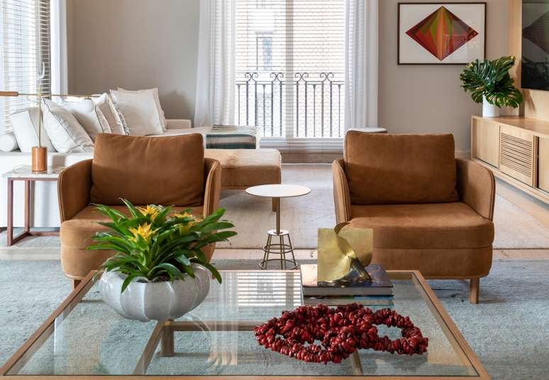 Uma das fun&ccedil;&otilde;es desta mesa de vidro &eacute; dar vis&atilde;o para o tapete. Para a decora&ccedil;&atilde;o nesse living, foram adicionados um vaso de murano que recebeu uma brom&eacute;lia e livros de arte que apoiam uma escultura.