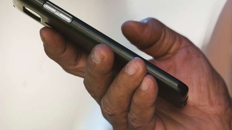 Imagem mostra uma mão negra segurando um celular.