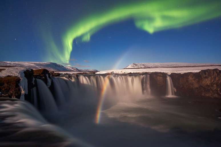 A aurora boreal e um arco-íris lunar visto acima da cachoeira Godafoss, na Islândia