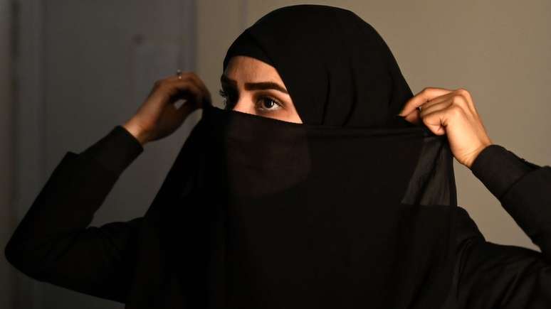 A apresentadora afegã da rede de notícias 1TV, Lima Spesaly, se prepara para cobrir o rosto com um véu antes de uma transmissão ao vivo