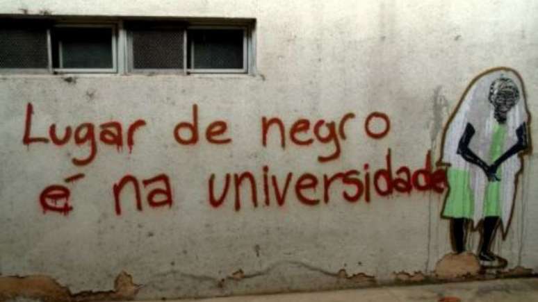 Imagem mostra um muro com a frase "lugar de negro é na universidade".