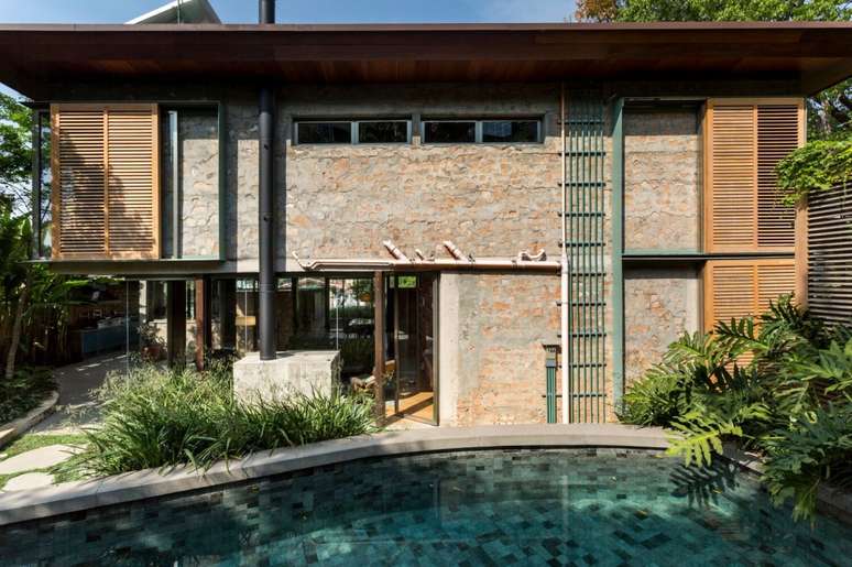 Lateral da casa com paredes de entulho em frente &agrave; piscina e ao jardim.