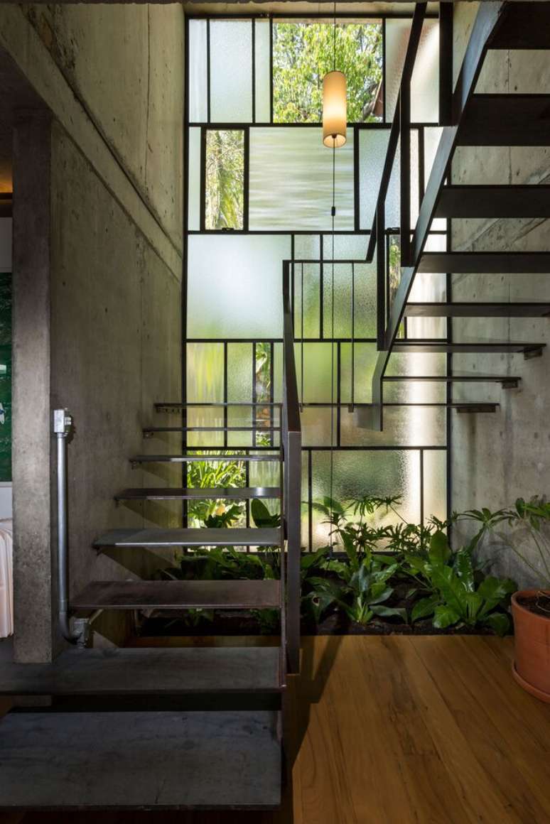 Escada met&aacute;lica interna tem parede de vitral que amplia a luz natural e permite manter um jardim de inverno.