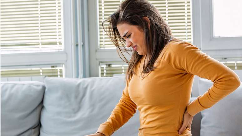 Mulher com dor nas costas sentada em sofá