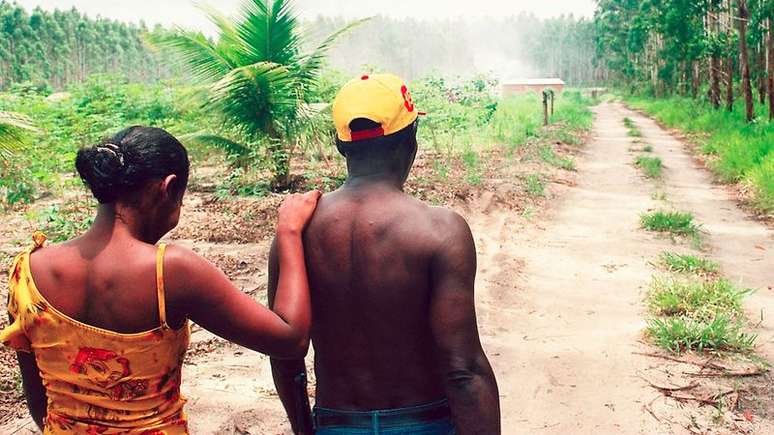 Imagem de dois quilombolas, de costas, em frente a uma estrada de terra.
