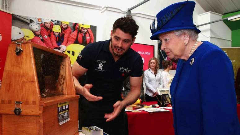 A rainha Elizabeth observando abelhas em uma colmeia em um evento do Prince's Trust