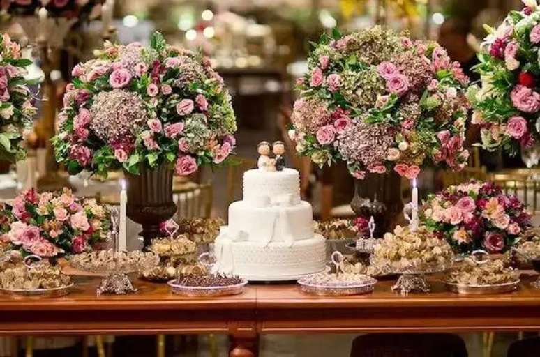 24. Decora&ccedil;&atilde;o de mesa de casamento bem cl&aacute;ssica com muitas flores e bolo branco