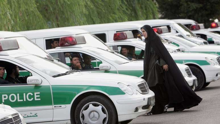 Policial iraniana de moralidade passa por veículos policiais antes da repressão às mulheres que violam o código de vestimenta islâmico em Teerã (23 de julho de 2007)
