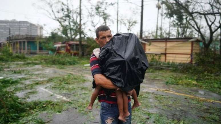 Um pai carrega seus filhos em Pinar del Río após a passagem do furacão.