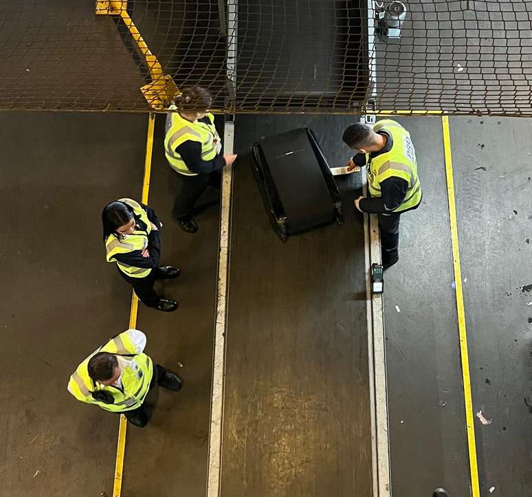 Funcion&aacute;rios checam a etiqueta da bagagem.