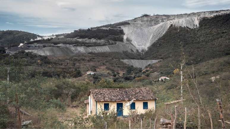 Imagem de uma casa quilombola. Ao fundo, a mina da Brazil Iron localizada na serra.