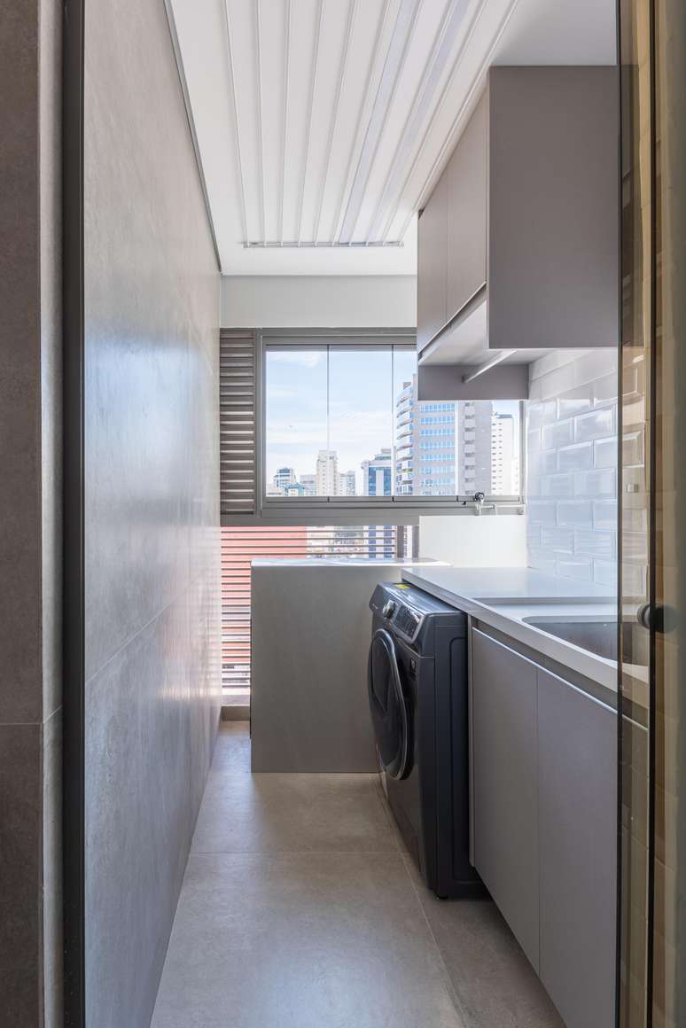 Nesta &aacute;rea de servi&ccedil;o com apenas 5,5 m&sup2;, uma parede inteira foi eleita para receber a marcenaria e embutir o tanque de inox na bancada de quartzo branco. Essa solu&ccedil;&atilde;o otimizou cent&iacute;metros e, no m&oacute;vel, o morador conseguiu armazenar todos os itens de limpeza e roupas para lavar| Projeto Bruno Moraes Arquitetura.