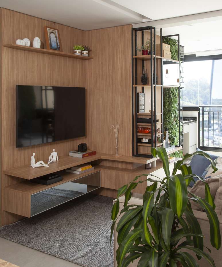 Essa sala, que antes n&atilde;o era integrada com a varanda, ganhou uma nova sensa&ccedil;&atilde;o depois da retirada das portas que delimitavam as &aacute;reas. Para descartar qualquer poss&iacute;vel sensa&ccedil;&atilde;o de segrega&ccedil;&atilde;o, a marcenaria vem desde a varanda e continua pelo estar, tornando-se o rack/painel da TV | Projeto Bruno Moraes Arquitetura.