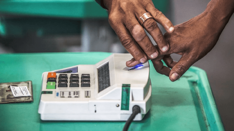 Imagem mostra mãos negras fazendo identificação biométrica para votar.