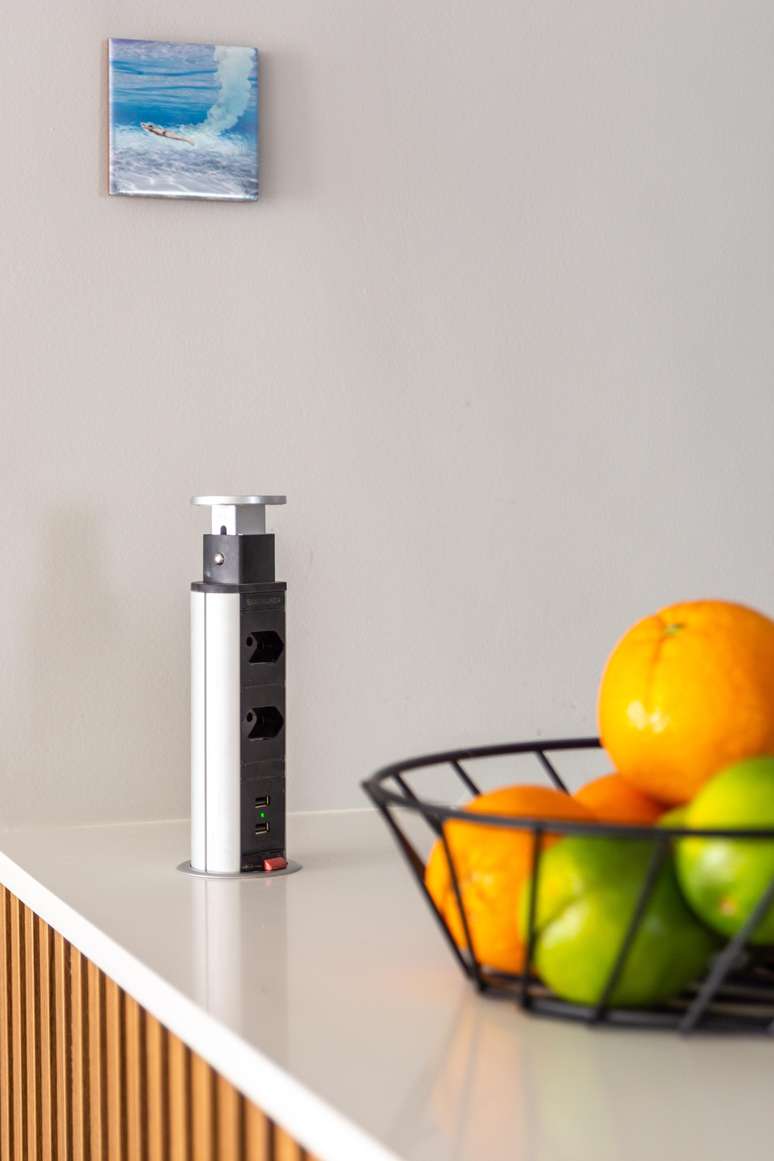 A torre de tomada embutida na superf&iacute;cie do quartzo do m&oacute;vel amadeirado &eacute; muito &uacute;til e permite conectar mais de um eletrodom&eacute;stico ao mesmo tempo, como uma cafeteira para servir o caf&eacute; da manh&atilde;, liquidificador para preparar uma receita na bancada ou carregar o celular | Projeto Bruno Moraes Arquitetura.