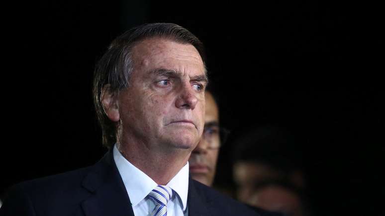 Fotografia colorida mostra Jair Bolsonaro com um terno preto em frente a um fundo escuro