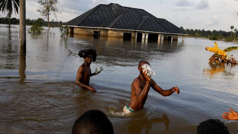 Moradores atravessam água após uma grande enchente na comunidade de Obagi, estado de Rivers, Nigéria