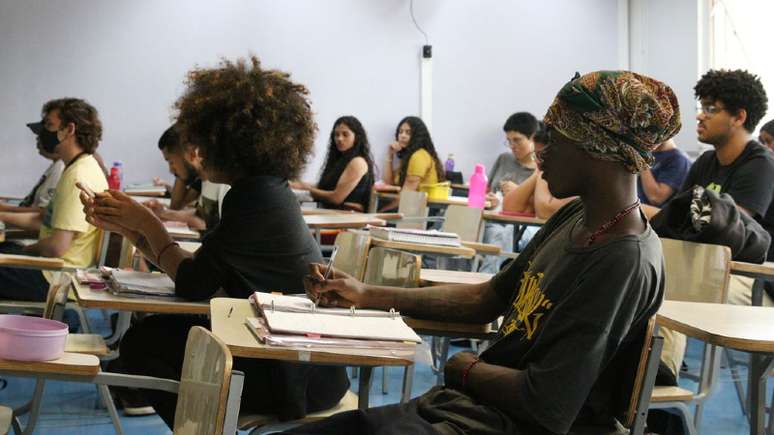 Estudantes negros aparecem em primeiro plano fazendo o Enem. Mais ao fundo outros estudantes brancos realizam as provas