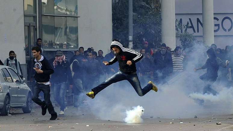 Redes sociais s&atilde;o uma ferramenta importante para manifestantes na Tun&iacute;sia. Nesta foto, um manifestante desvia de uma bomba de g&aacute;s lacrimog&ecirc;neo durante uma manifesta&ccedil;&atilde;o ap&oacute;s a morte de um l&iacute;der da oposi&ccedil;&atilde;o em 2013.