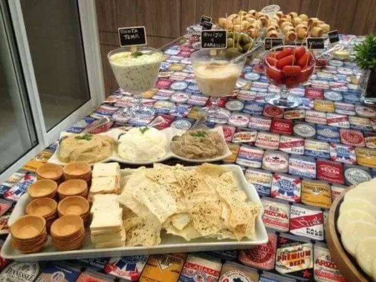 24- No ch&aacute; de casa nova, a mesa tem toalha com estampas de latas de cerveja. Fonte: Na Cozinha da Bruninha