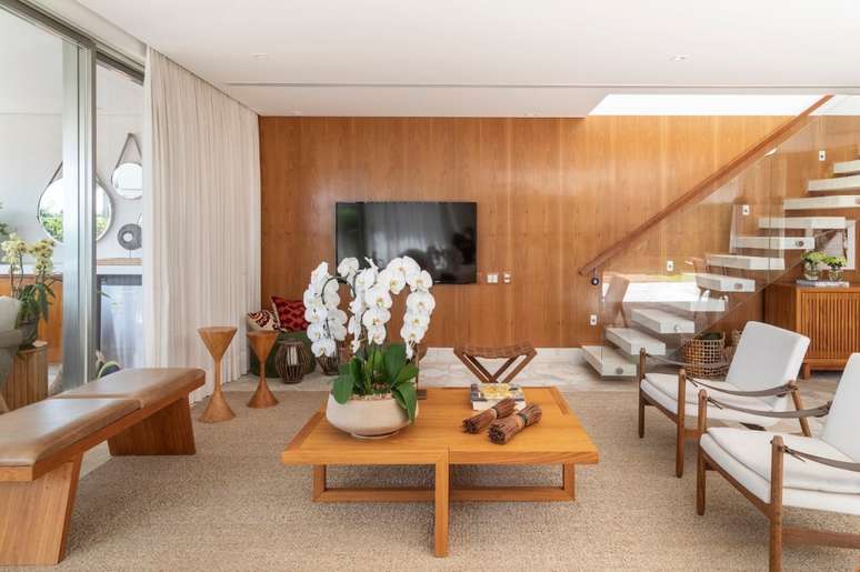 A mesa de centro acompanha o &lsquo;mood&rsquo; do ambiente, todo projetado com tons amadeirados. Na decora&ccedil;&atilde;o do m&oacute;vel, destaque para o lindo vaso cer&acirc;mico com orqu&iacute;deas brancas.