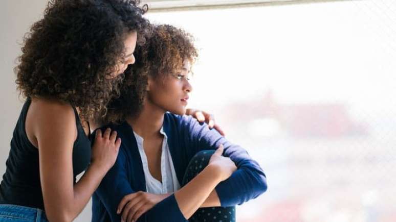 Imagem mostra pessoas negras, duas mulheres que se consolam.