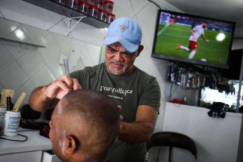 Um olho no cliente e outro no jogo: barbeiro Valberto da silva, 48, não pode parar de trabalhar na Rua Catar