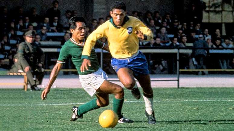 Imagem mostra Garrincha, com o uniforme da Seleção Brasileira, driblando adversário.