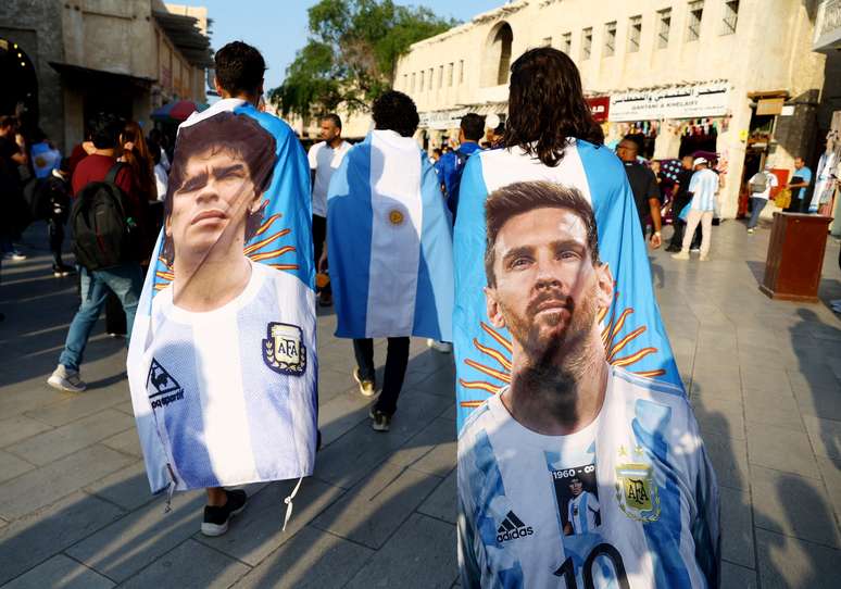 Torcedores argentinos carregam bandeiras com imagens dos ídolos Diego Maradona e Lionel Messi nesta terça-feira, 13, no Catar.