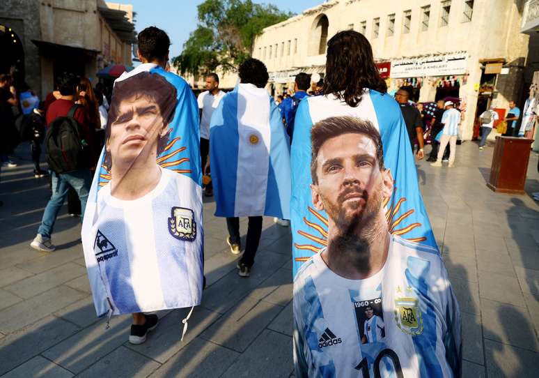 Torcedores argentinos carregam bandeiras com imagens dos ídolos Diego Maradona e Lionel Messi na terça-feira, 13, no Catar.