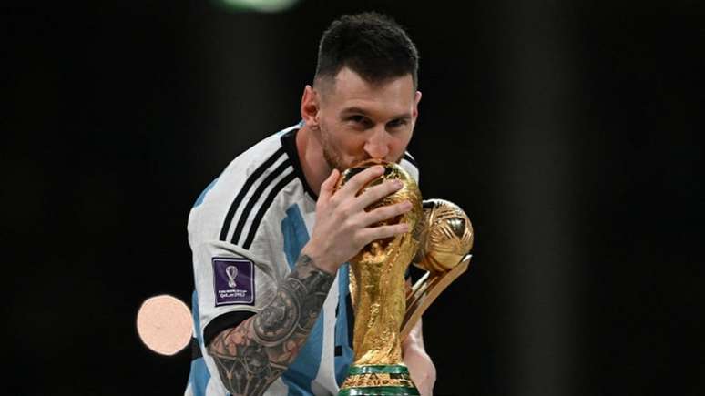 Messi beija a taça da Copa do Mundo enquanto segura o prêmio de craque do torneio 