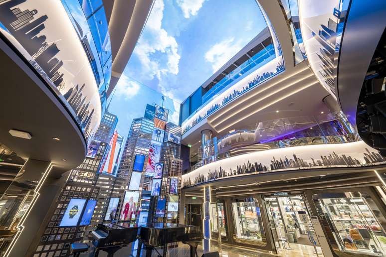 No corredor das lojas, um painel de LED projeta imagens da Times Square.