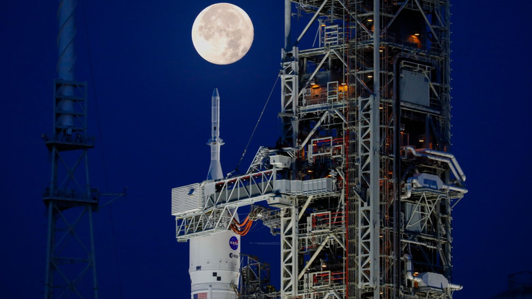 Imagem do nariz do foguete Artemis-i SLS com a cápsula Orion no pórtico de lançamento à luz da Lua