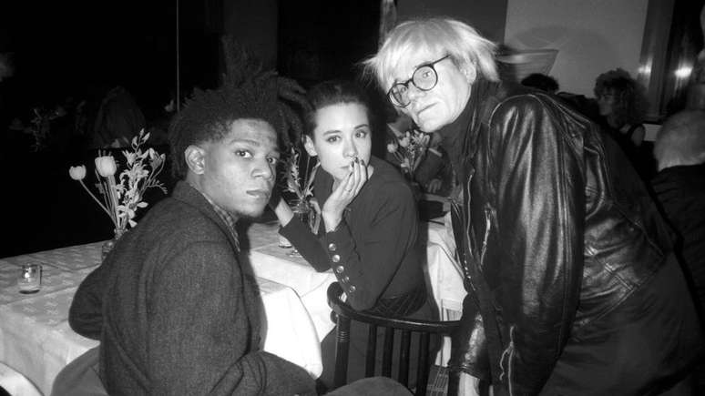 Na Nova York dos anos 1980, os artistas pl&aacute;sticos eram assediados pela imprensa como estrelas do rock. Basquiat e Warhol eram parte deste seleto grupo que era presen&ccedil;a constante em festas e coquet&eacute;is. Na foto, eles aparecem com a modelo Tina Chow