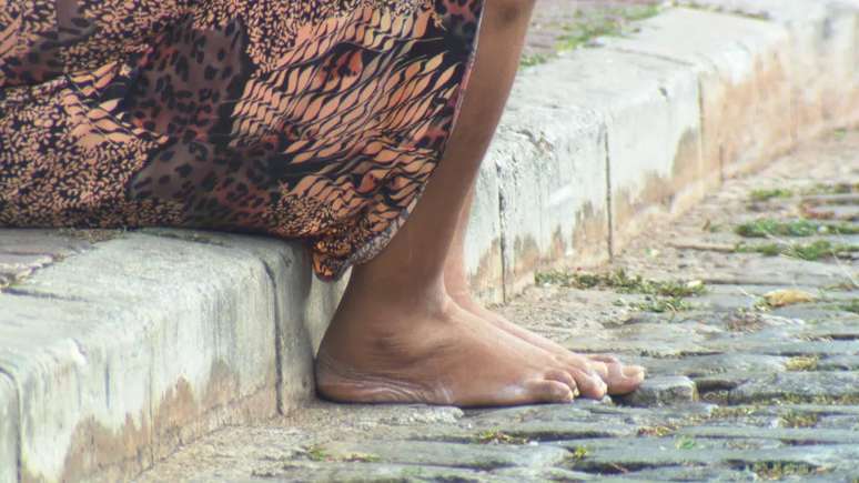 Imagem mostra os pés de uma mulher negra, moradora de rua.