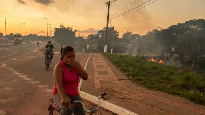 Em foto de julho de 2022, ciclistas passam perto de um foco de incêndio em Rio Branco (AC); queimadas urbanas são frequentes no Estado principalmente entre julho e setembro