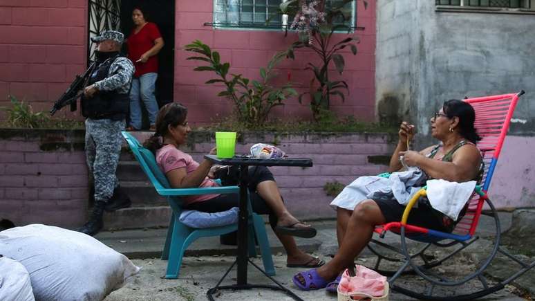 Mulheres bordam enquanto policial das forças salvadorenhas de Bukele patrulha a área