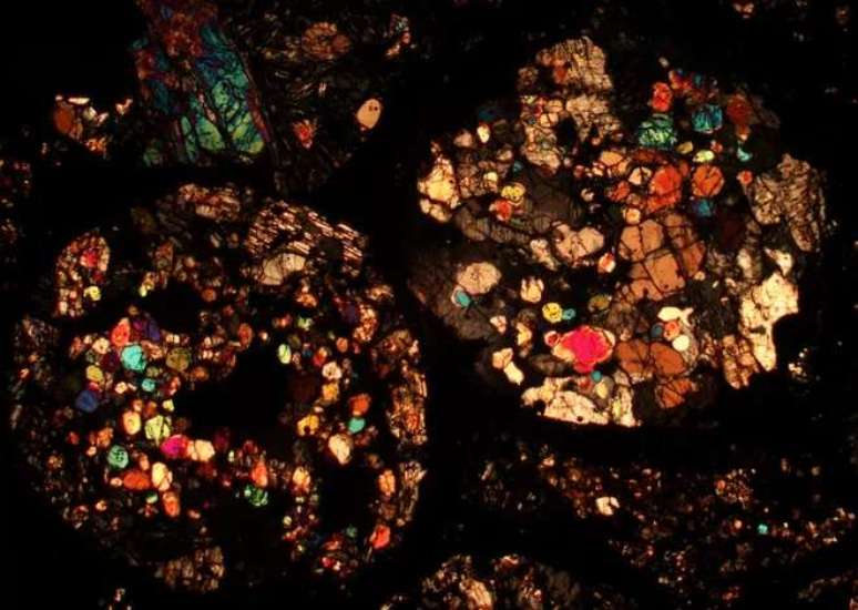Slice of meteorite observed under a microscope; the different colors represent the various minerals present (Image: Playback/Nicole Xike Nie) Slice of meteorite observed under a microscope; the different colors represent the various minerals present (Image: Playback/Nicole Xike Nie)