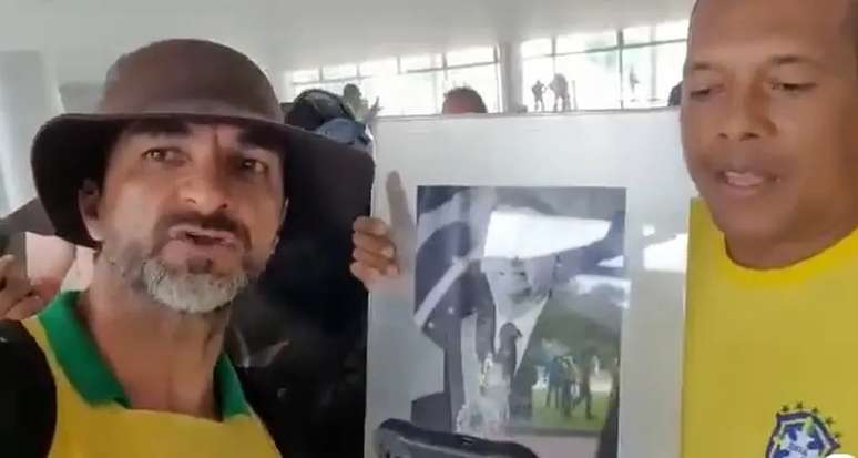 Alcimar postou um vídeo em que aparece ao lado de um homem vestido com a camisa da Seleção Brasileira segurando o quadro do ex-presidente Jair Bolsonaro.