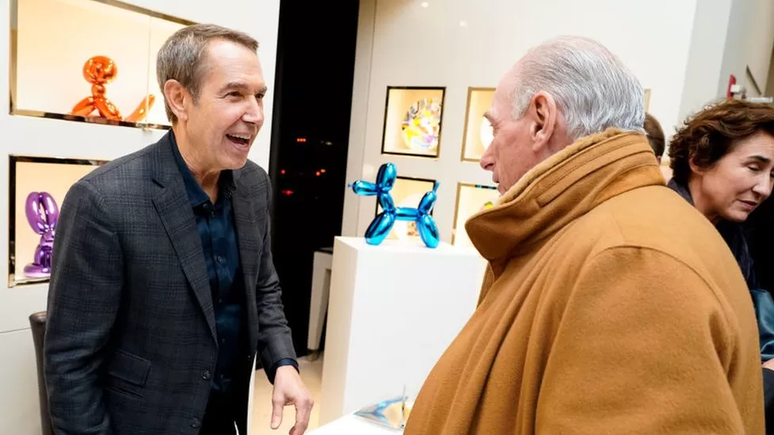 Jeff Koons (à esquerda) fala com um fã em um evento em 2021, com uma de suas estátuas azuis da série Balloon Dog ao fundo