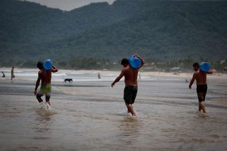 Galões de água são levados por voluntários para barco com donativos na praia de Maresias, no litoral norte