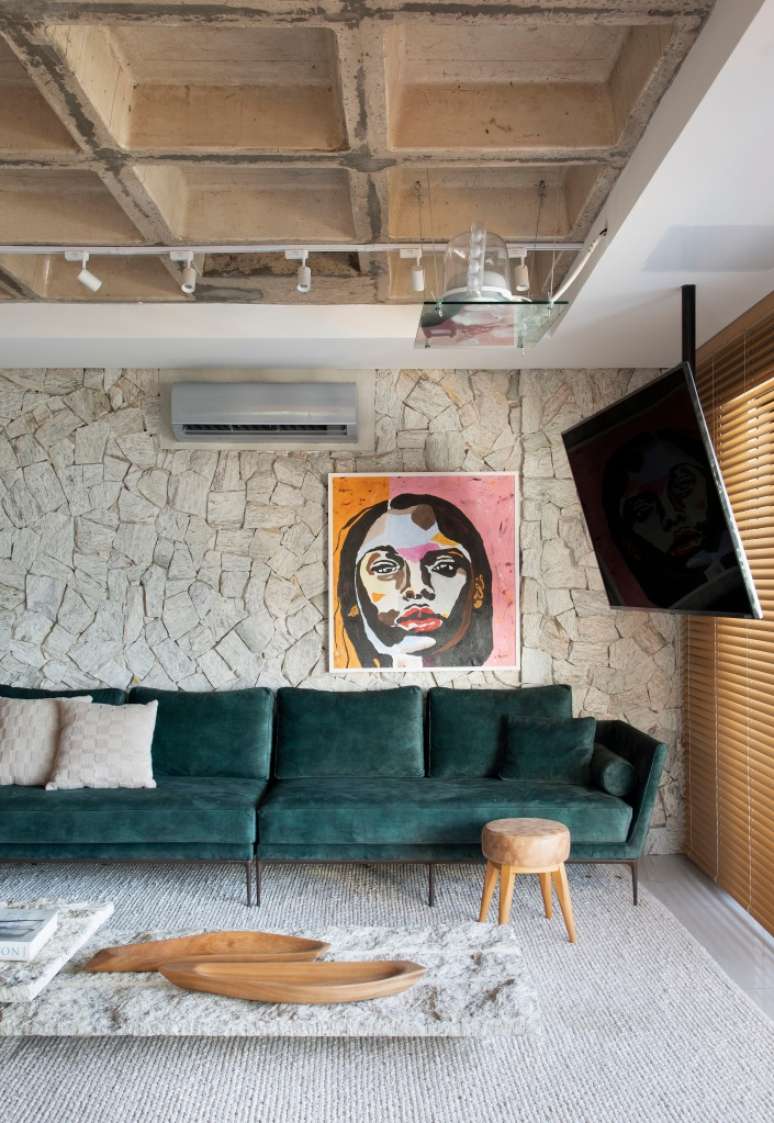 Sala de estar; sala de tv com parede de pedra, sof&aacute; verde e quadro.