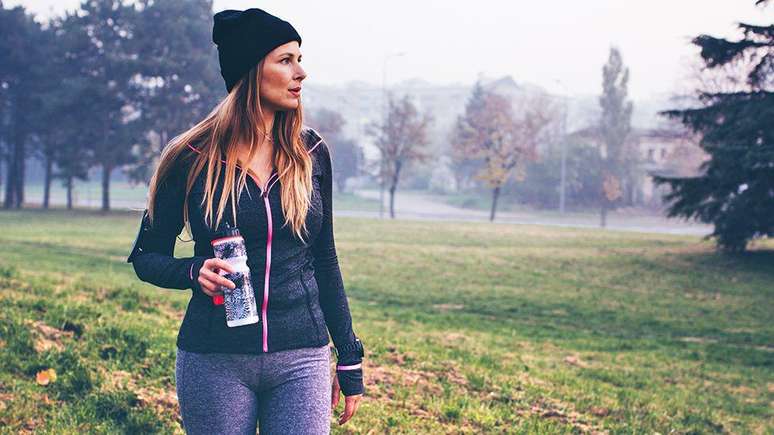 Mulher caminhando no parque com garrafa de água na mão durante o inverno