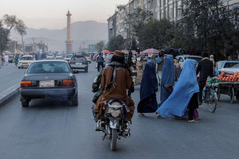 Mulheres de burca atravessam rua em frente a membros do Taliban em Cabul, no Afeganist&atilde;o