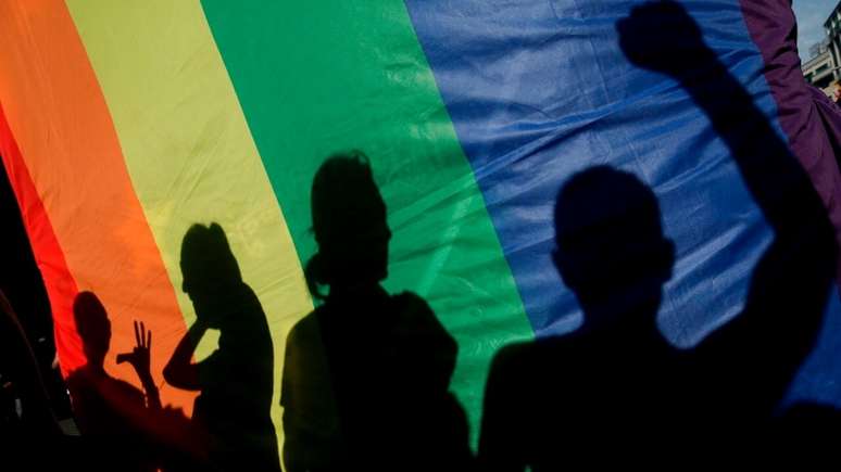 Imagem mostra sombra de pessoas em bandeira LGBTQIAP+.