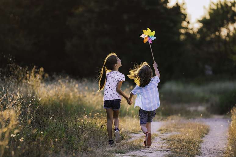 menina e menino correndo no campo de m&atilde;os dadas