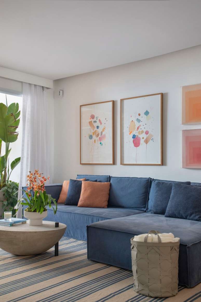 Sala com sof&aacute; L azul, tapete listrado e mesa de centro.