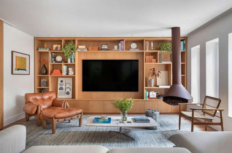 Sala de estar com painel de madeira com tv e nichos, poltrona Mole e lareira.
