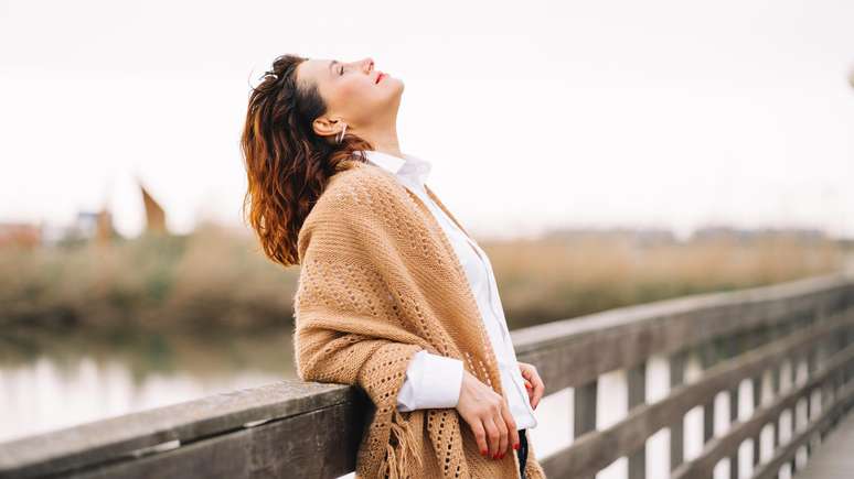 Mulher feliz com o rosto virado para o Sol sobre uma ponte