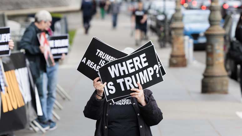 Do lado de fora do tribunal, em Nova York, mulher mostra cartaz: 'Onde está Trump?'